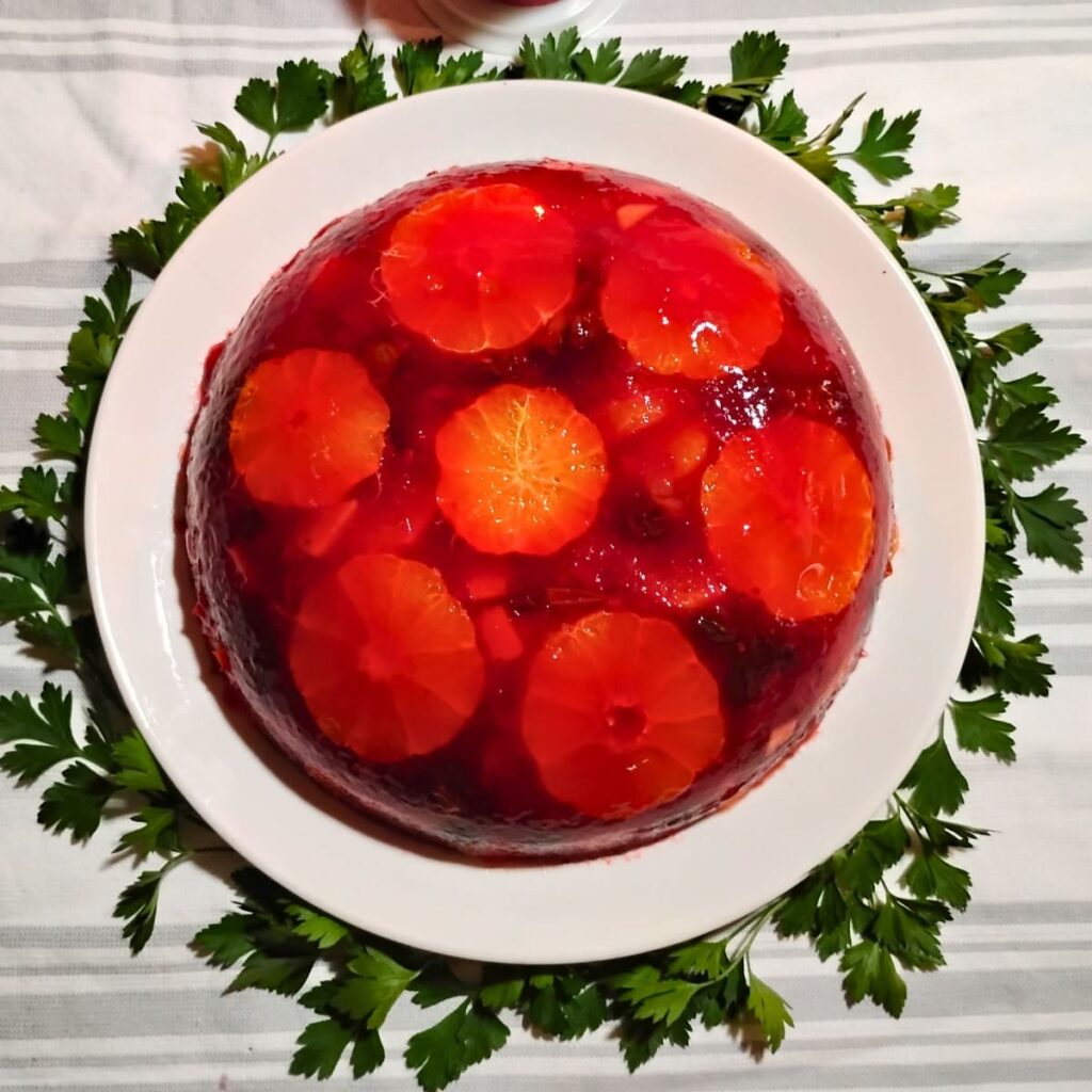 photo of a congealed cranberry and orange salad made with beef gelatin and hibiscus tea. served on a white plate surrounded with parsley.