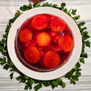 photo of a congealed cranberry and orange salad made with beef gelatin and hibiscus tea. served on a white plate surrounded with parsley.