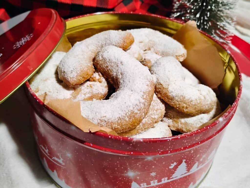 vanillekipferl in a christmas tin with a lid leaning on it.