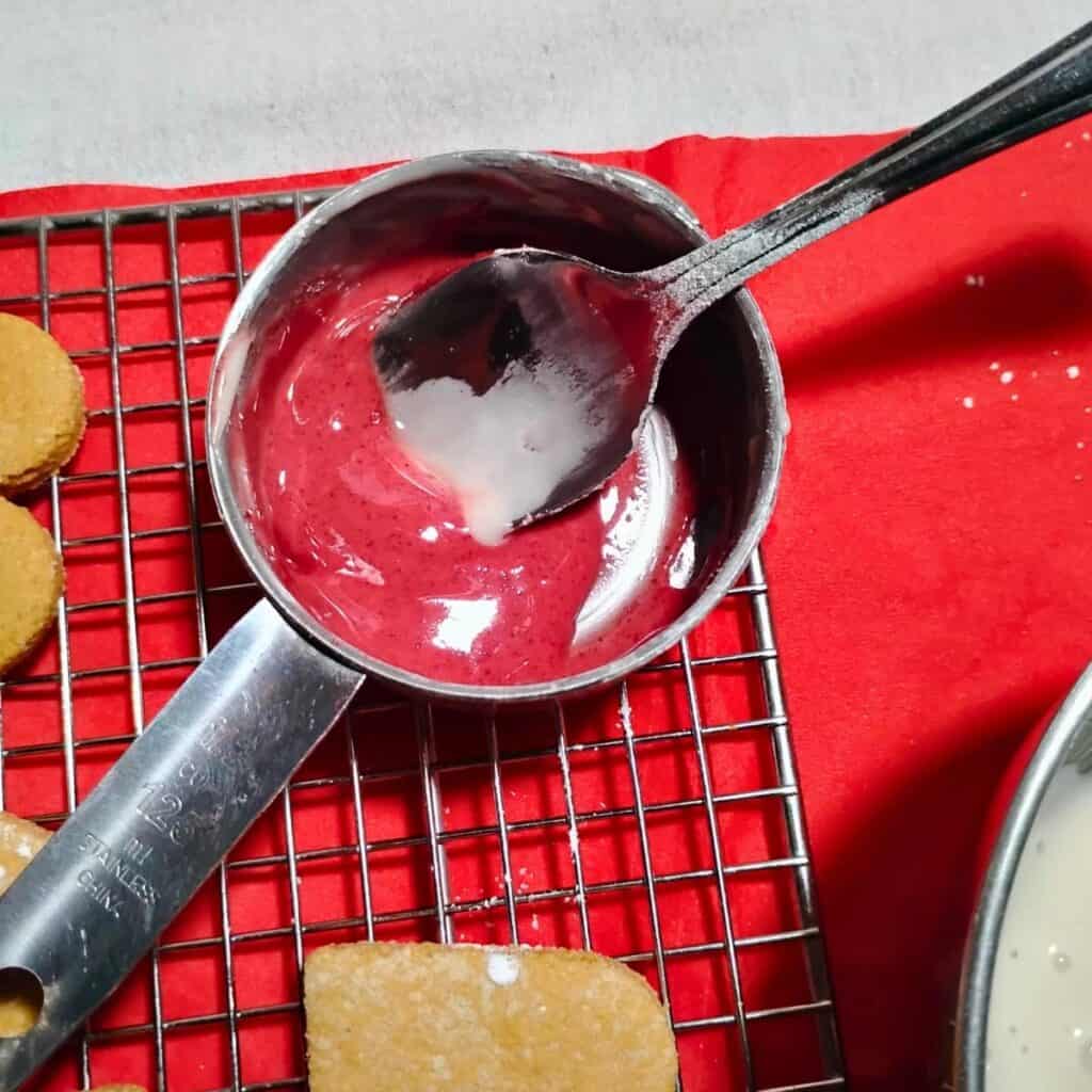 a measuring cup with a small amount of beet colored icing.
