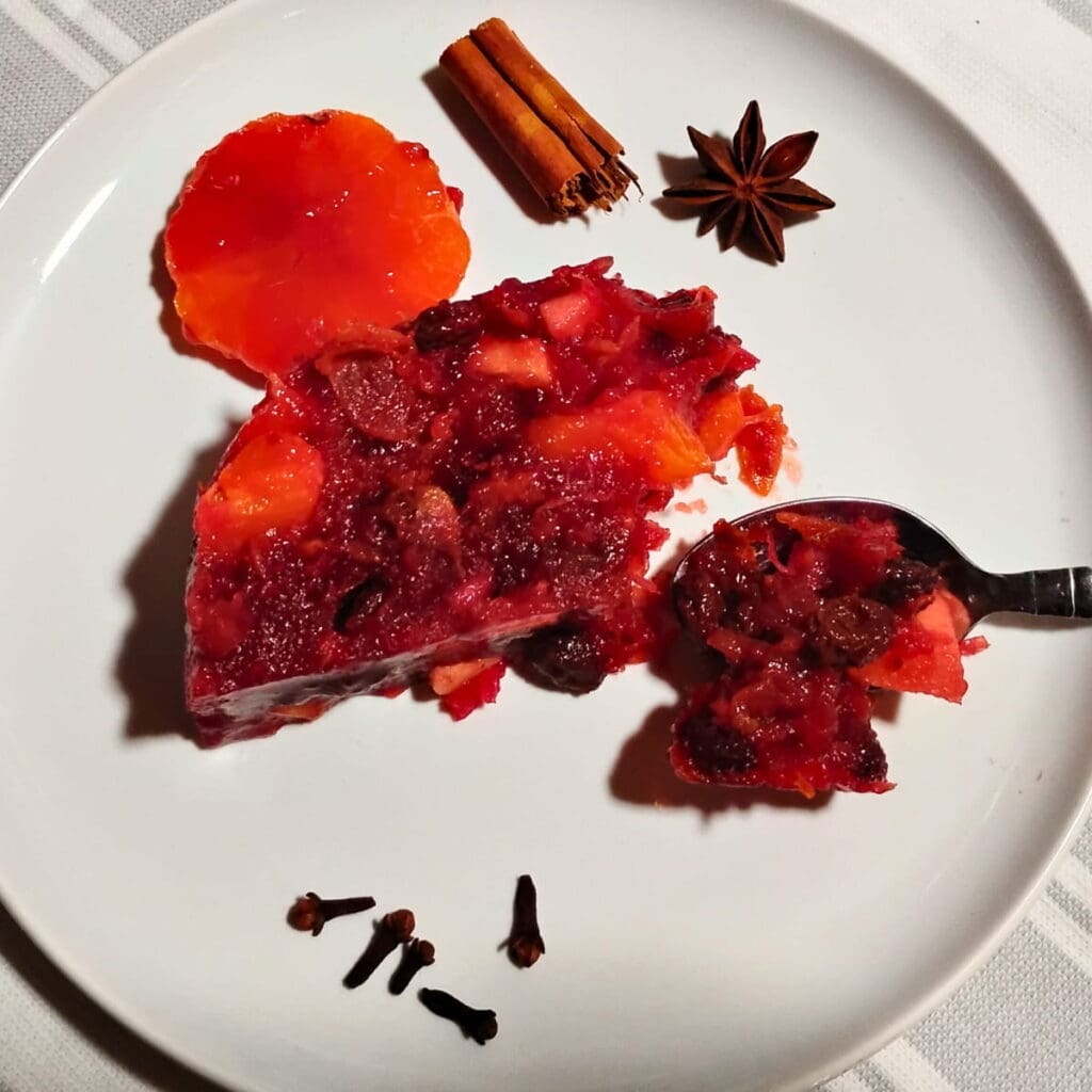 photo of a slice of the cranberry orange salad on a plate with a spoon removing some. There are some spices on the plate for decoration.