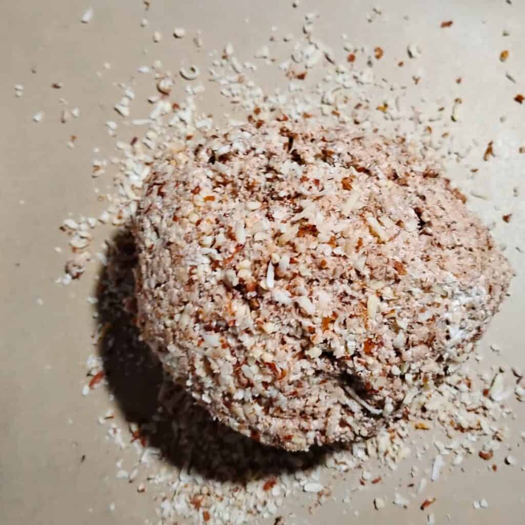 Almond meringue dough laying on a piece of parchment with nuts below and on top of it.