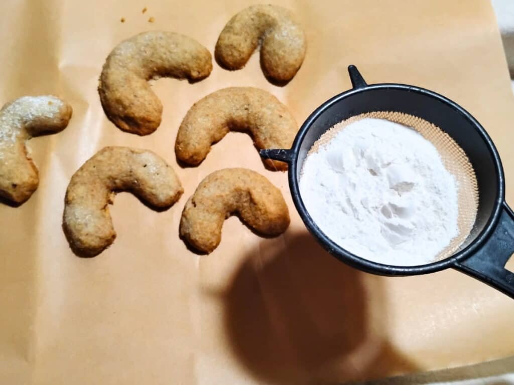 a sieve is filled with powdered sugar ready to dust the cookies below it.