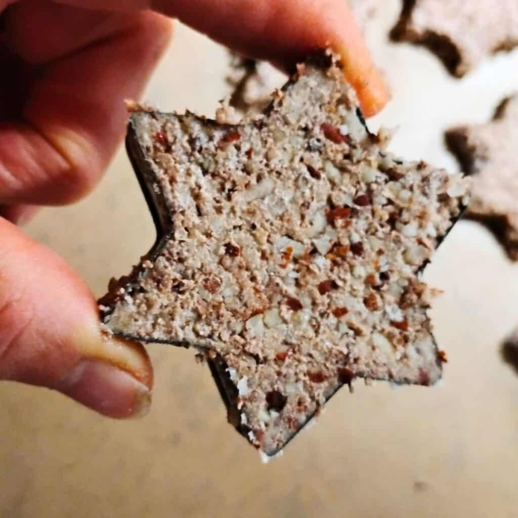 closeup of a person's hand holding a cinnamon star inside a star shaped cutter to get placed on the cookie sheet.
