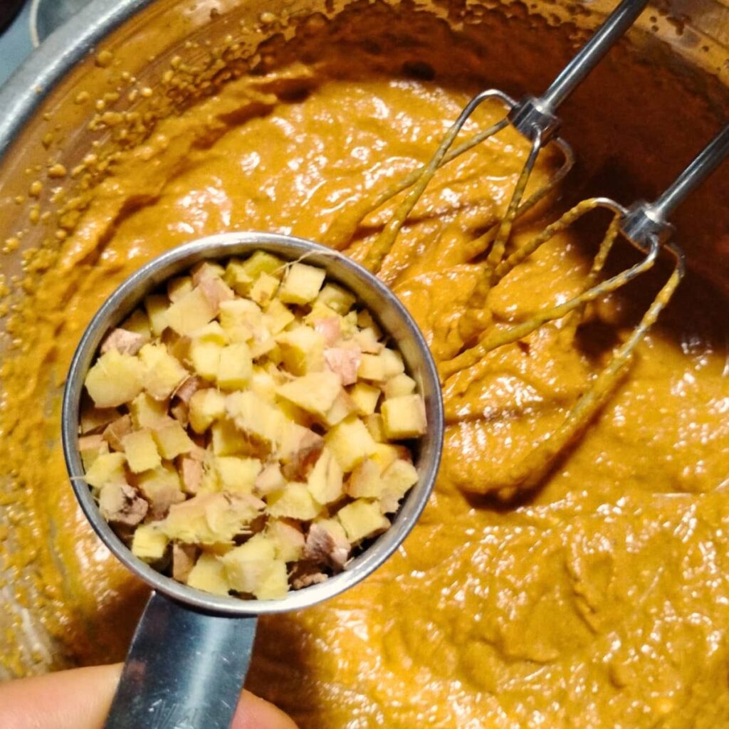 chopped ginger is added to some batter inside a bowl with beaters in it.