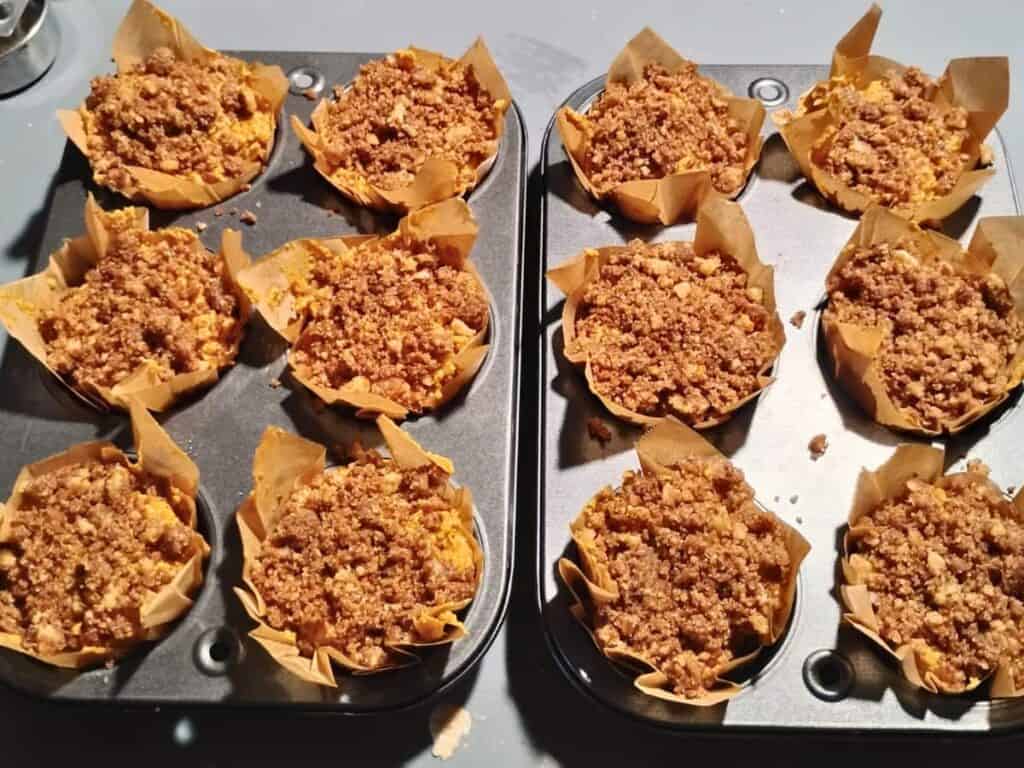 two muffin trays with unbaked muffin dough topped with streusel inside homemade tulip liners.