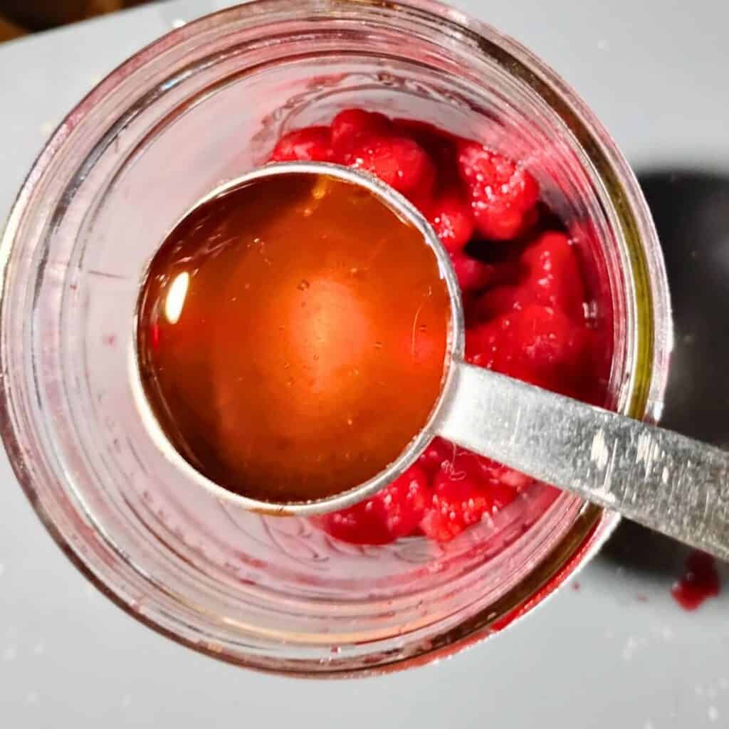 honey is ready to get added to some raspberries in a wide mouth canning jar.