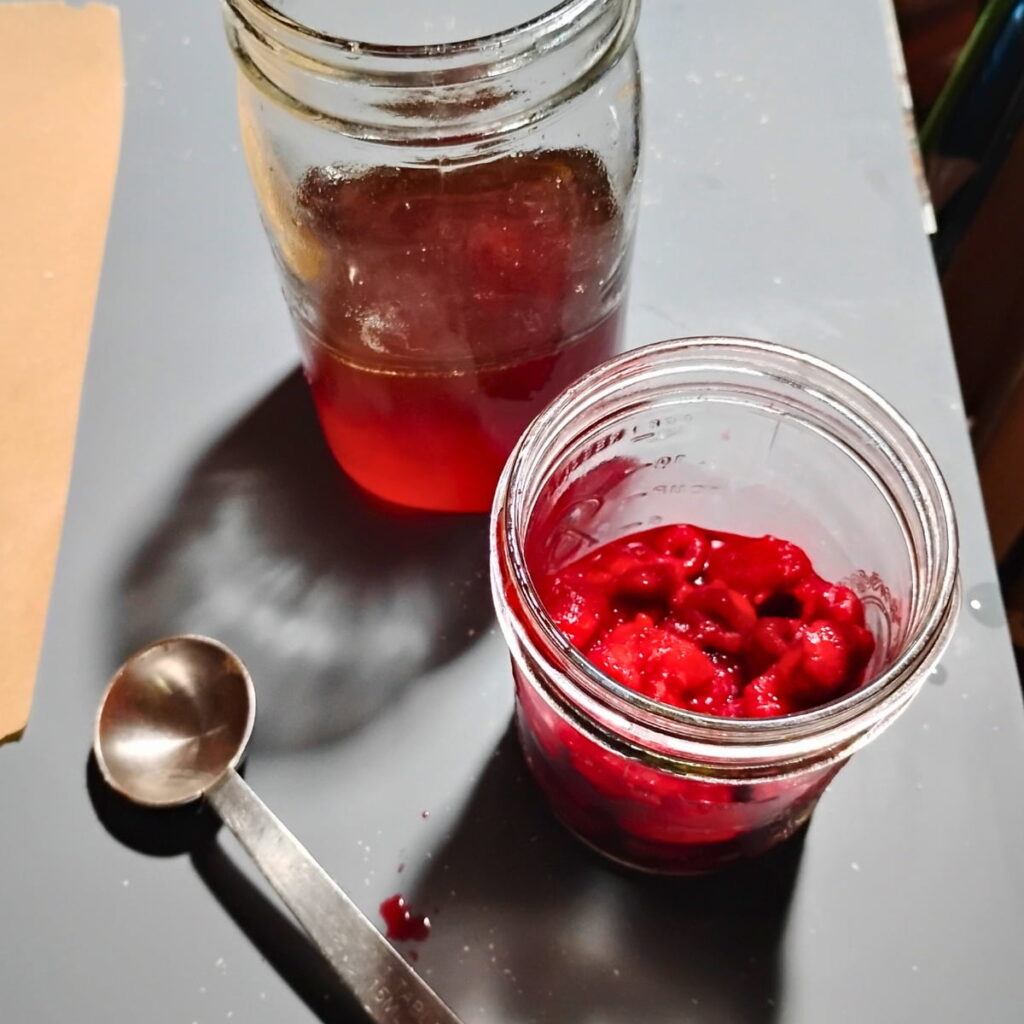 a jar with honey, a jar with frozen raspberries and a measuring spoon next to it.