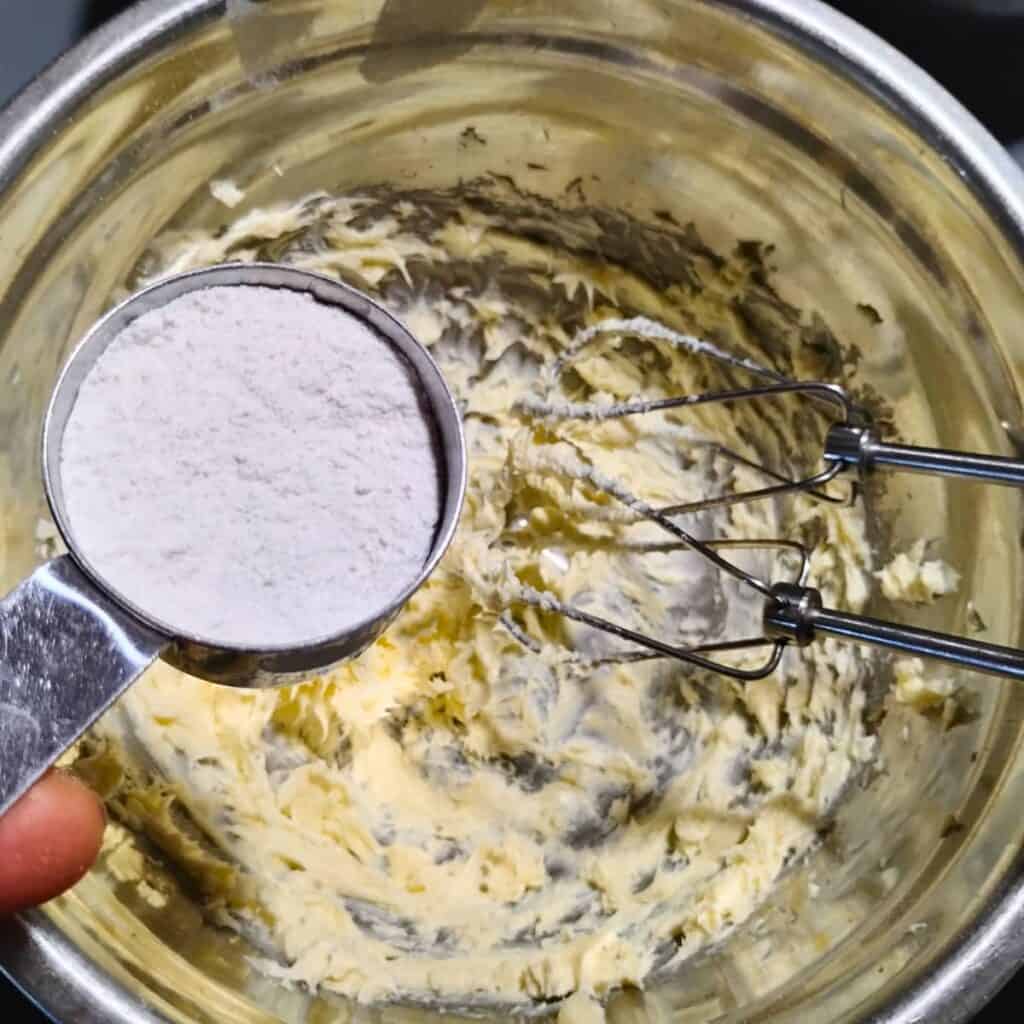 a bowl with creamed butter. powdered sugar is added to it. There are two beaters in the bowl that belong to a mixer.