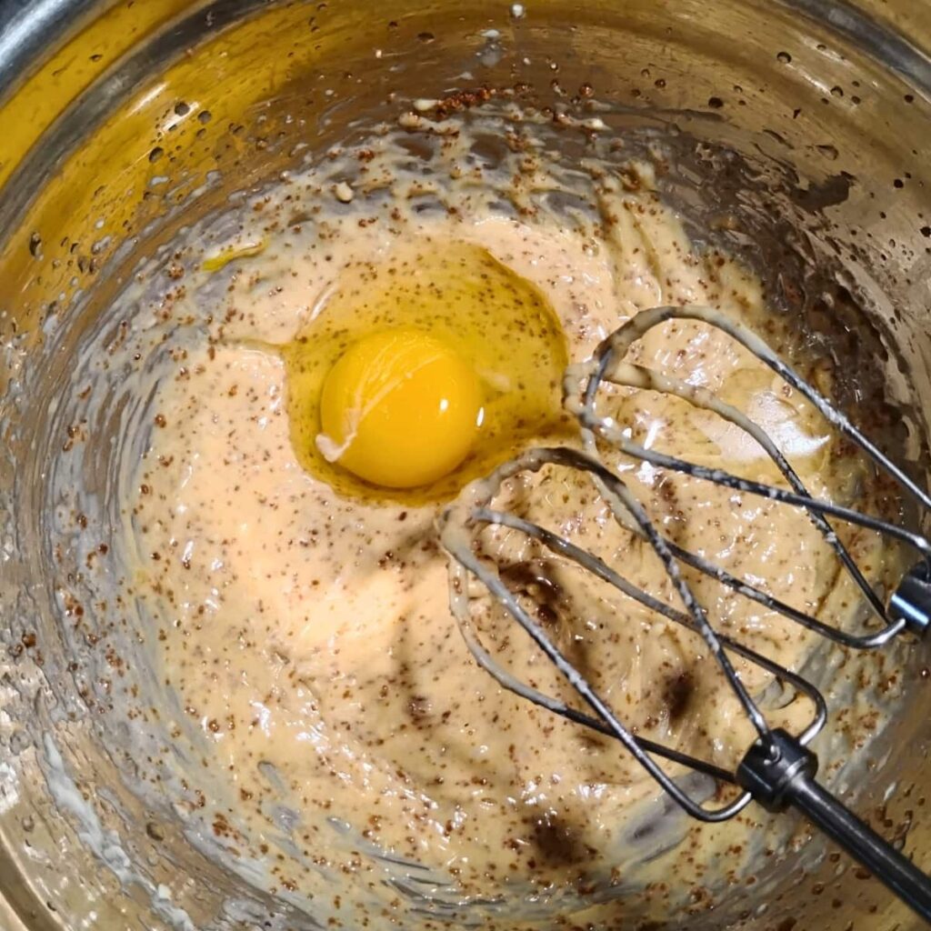 a bowl with some oil, butter, and panela sugar creamed and an egg added. there are beaters of a hand mixer showing.