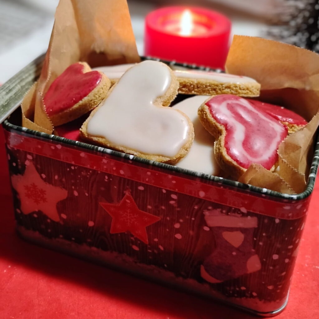 a christmas tin filled with zitronenherzen, lemon heart cookies. there is a candle behind it. 