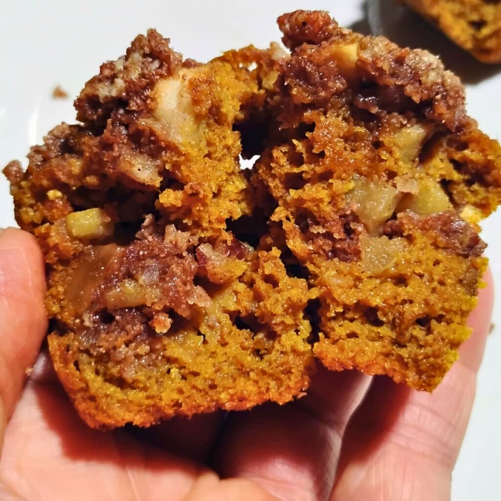 a hand is holding half a muffin to show the texture.