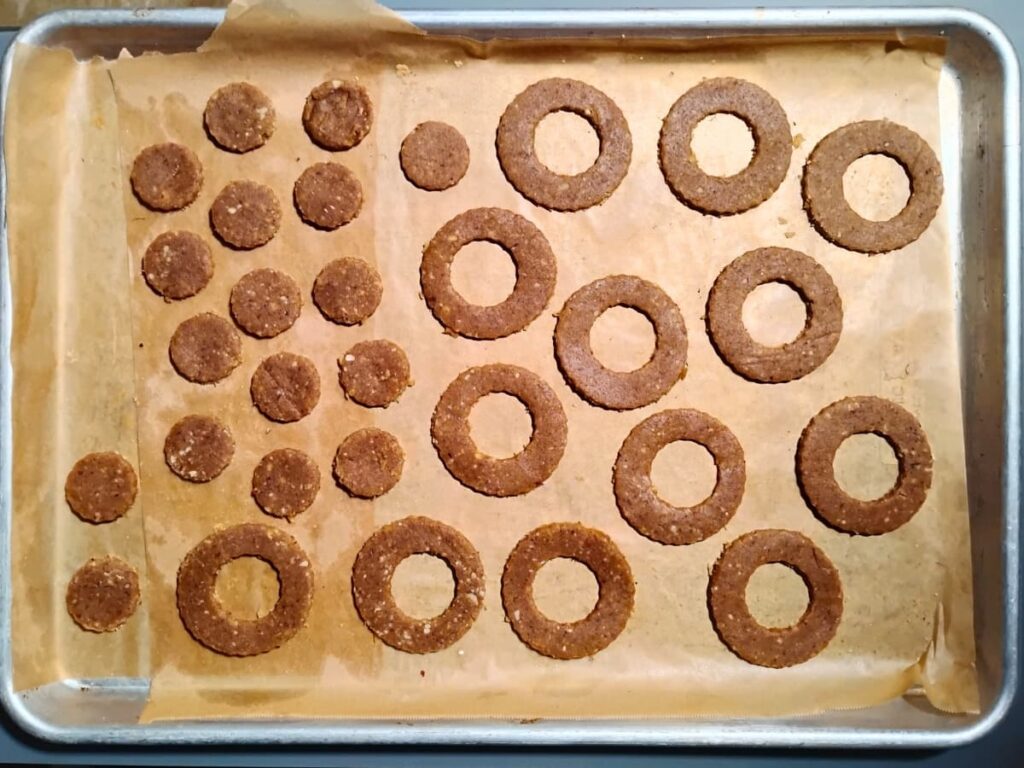 A baking sheet filled with cutout cookie rings and small cutout shapes that used to be the centers of the rings.
