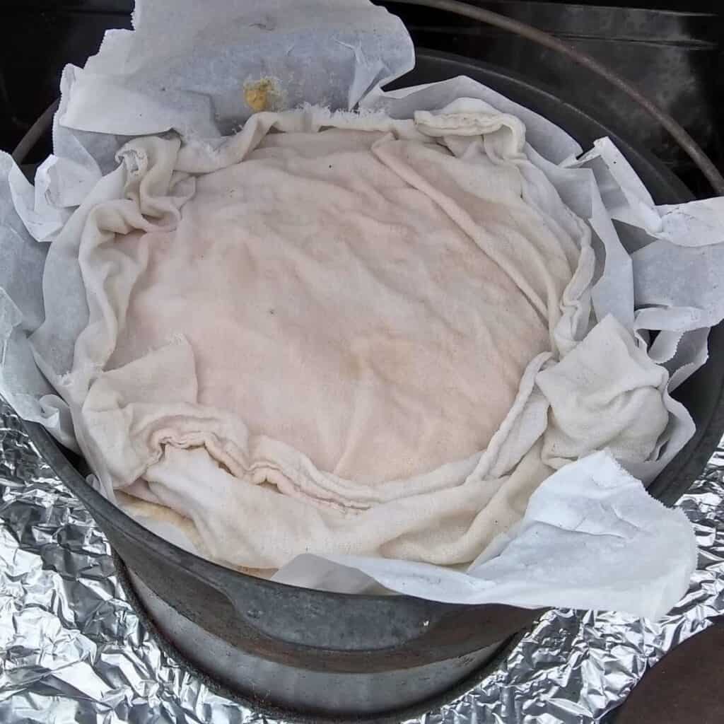 A dutch oven filled with bread dough and a wet cloth covering it.