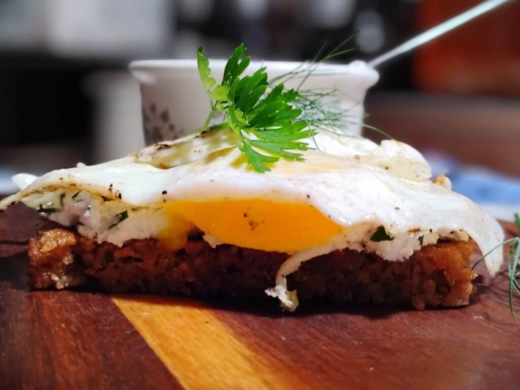 photo of a slice of sourdough rye bread on a cutting board with creamy cheese and herbs and fried egg on top. 