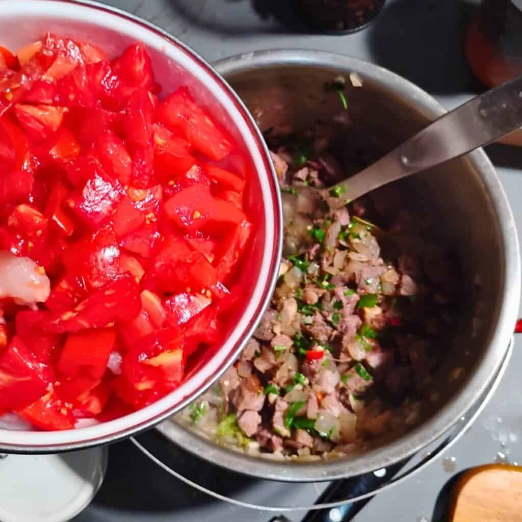 tomatoes and shrimps are added to the ingredients in the pot.