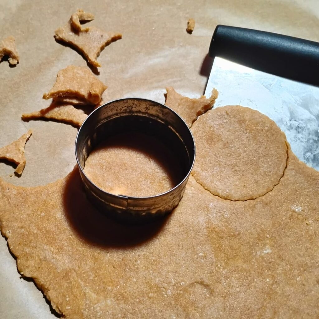 photo of cookies getting cut out of rolled out dough. A bench knife is getting slid under the cutouts for easier transfer to the baking sheet.