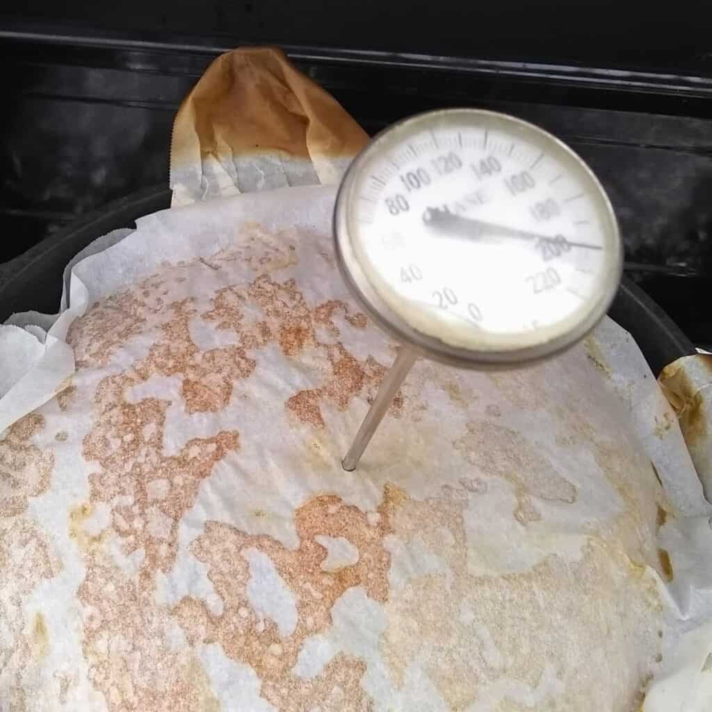 thermometer stuck in a parchment covered bread loaf in a Dutch oven.