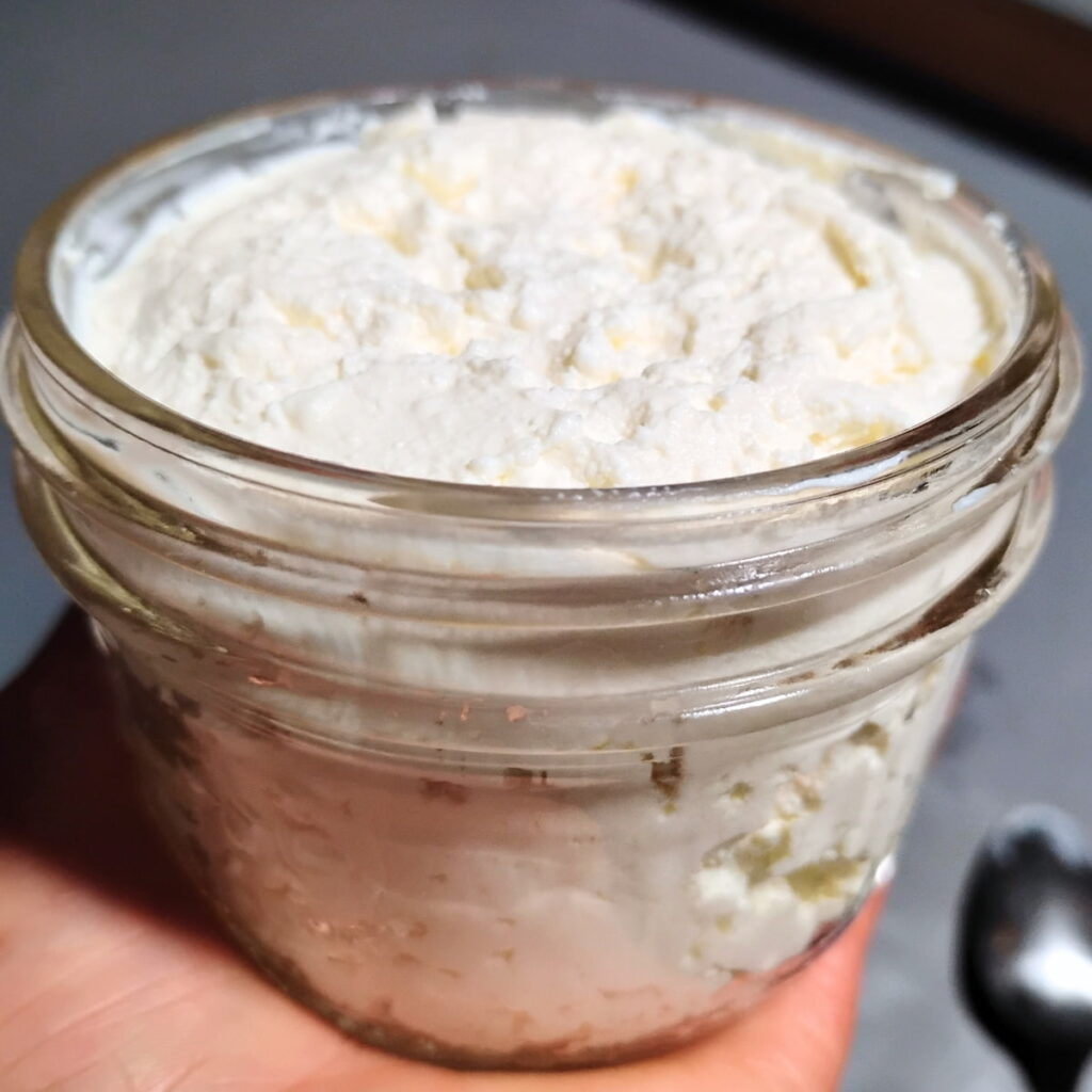 a hand is holding a jar filled with fresh cheese made with sourdough starter. 