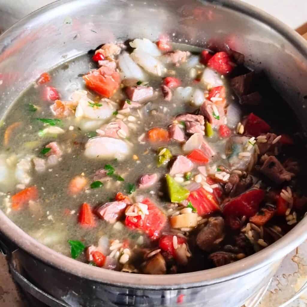 A pot filled with ham jambalaya ingredients and broth, getting heated for cooking it.