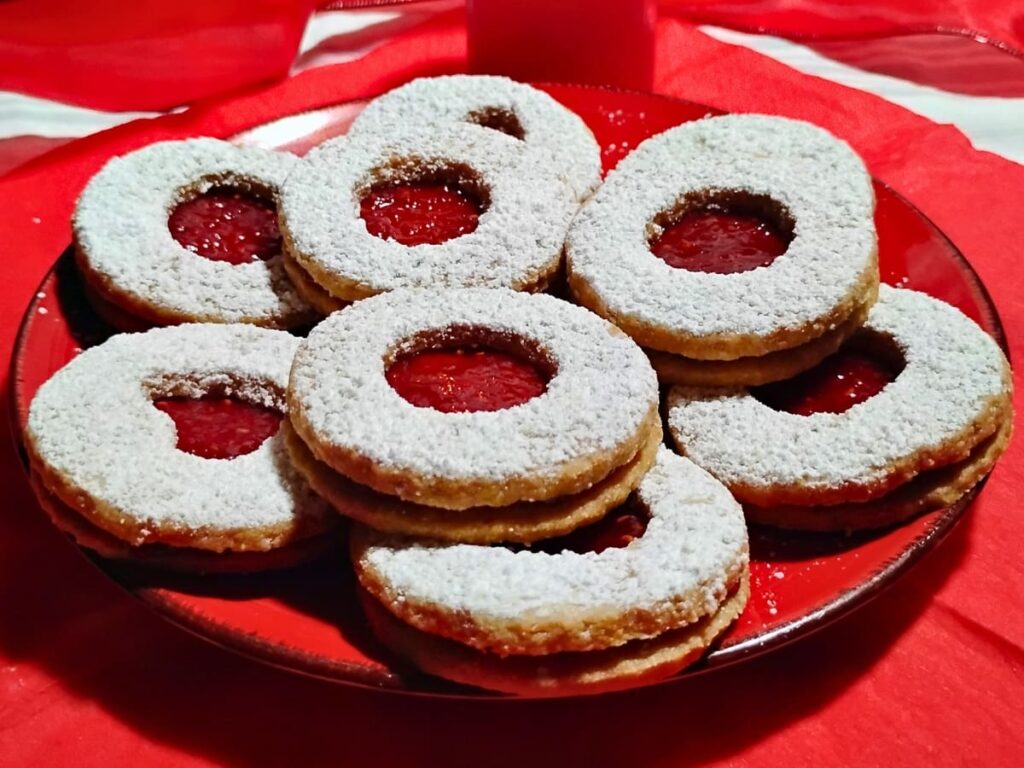 plate full of linzer cookies filled with raspberry jam and red linzer eyes.