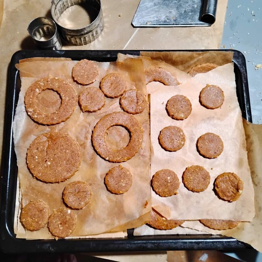 A consolidated bunch of cookies stacked onto a small cookie sheet, layers separated with parchment. The cookies are getting chilled this way to better retain their shape when baking. They are placed onto bigger cookie sheets once chilled.