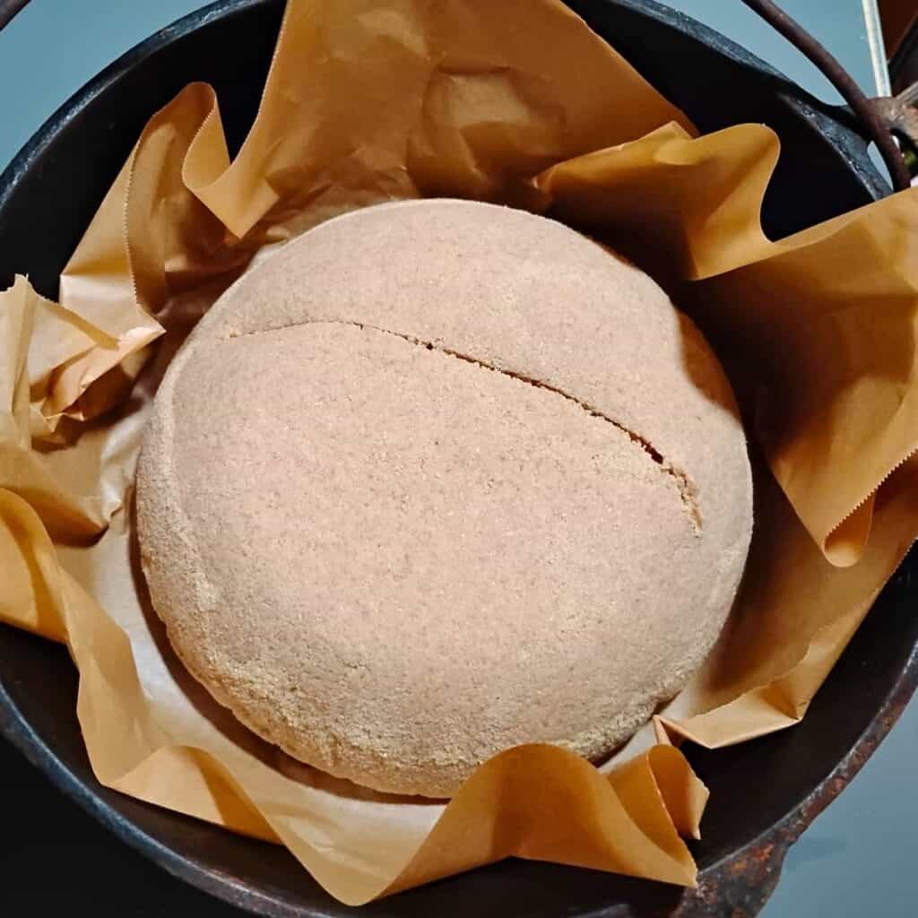 A dutch oven lined with parchment and a bread loaf inside it with a slit. 