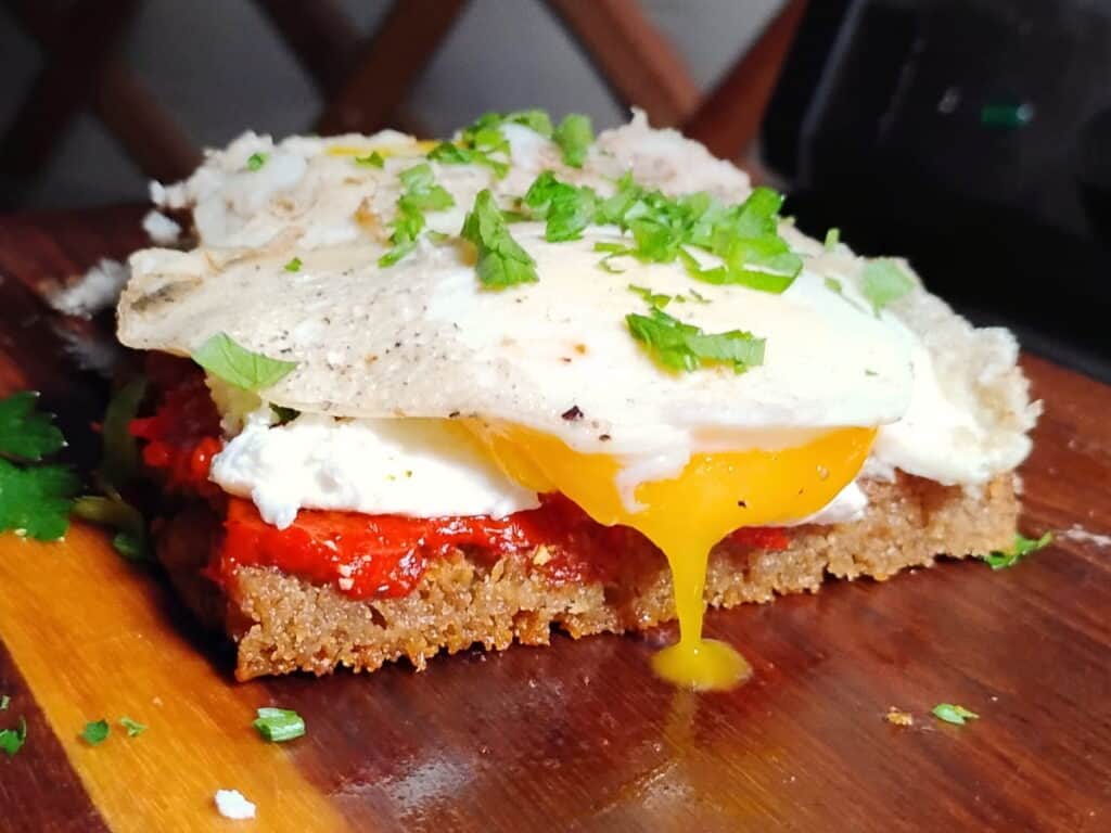 sandwich on a cutting board. A fried slice of sourdough rye bread topped with ajvar, feta cheese, and fried eggs. 
