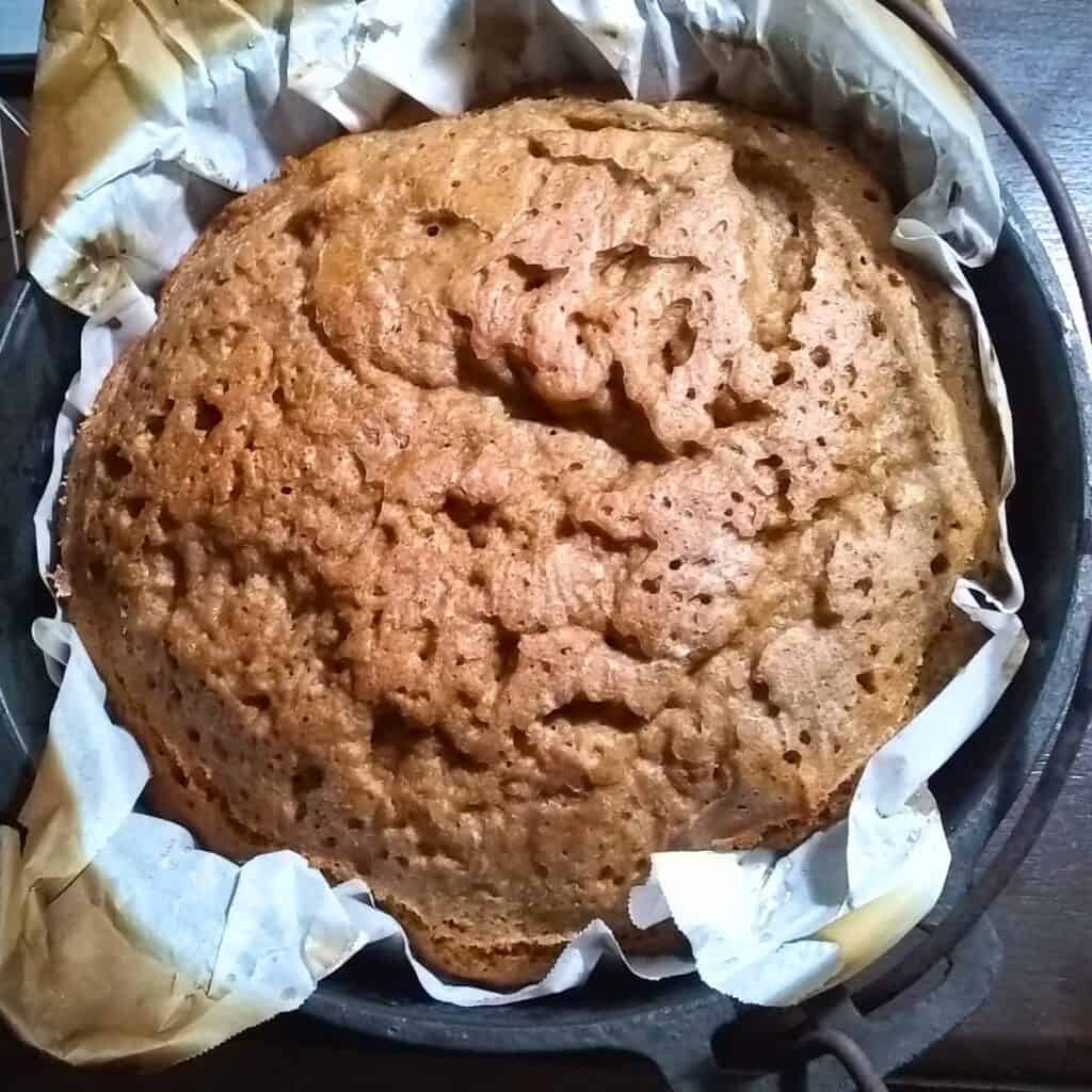 a fresh baked loaf of sourdough rye bread in a dutch oven inside parchment. 