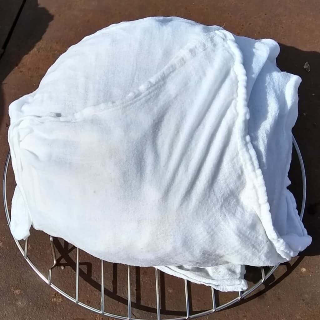 breadloaf wrapped in a floursack towel on a cooling rack.