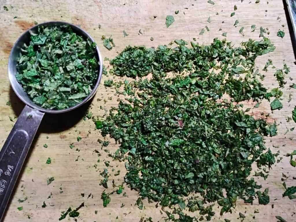 chopped mint on a cutting board with a quarter cup measure filled with more chopped mint. 
