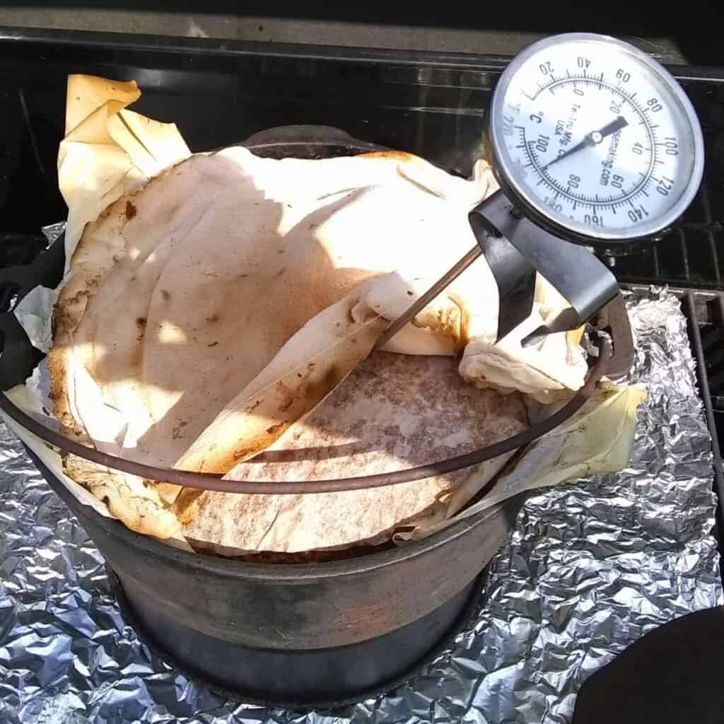 photo shows a dutch oven with a breadloaf that's covered with cloth and a thermometer stuck in the middle of it.
