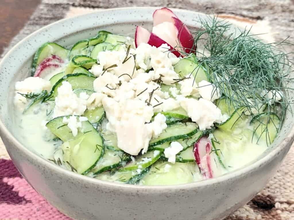 bowl filled with cucumber salad and dill, topped with feta cheese chunks.