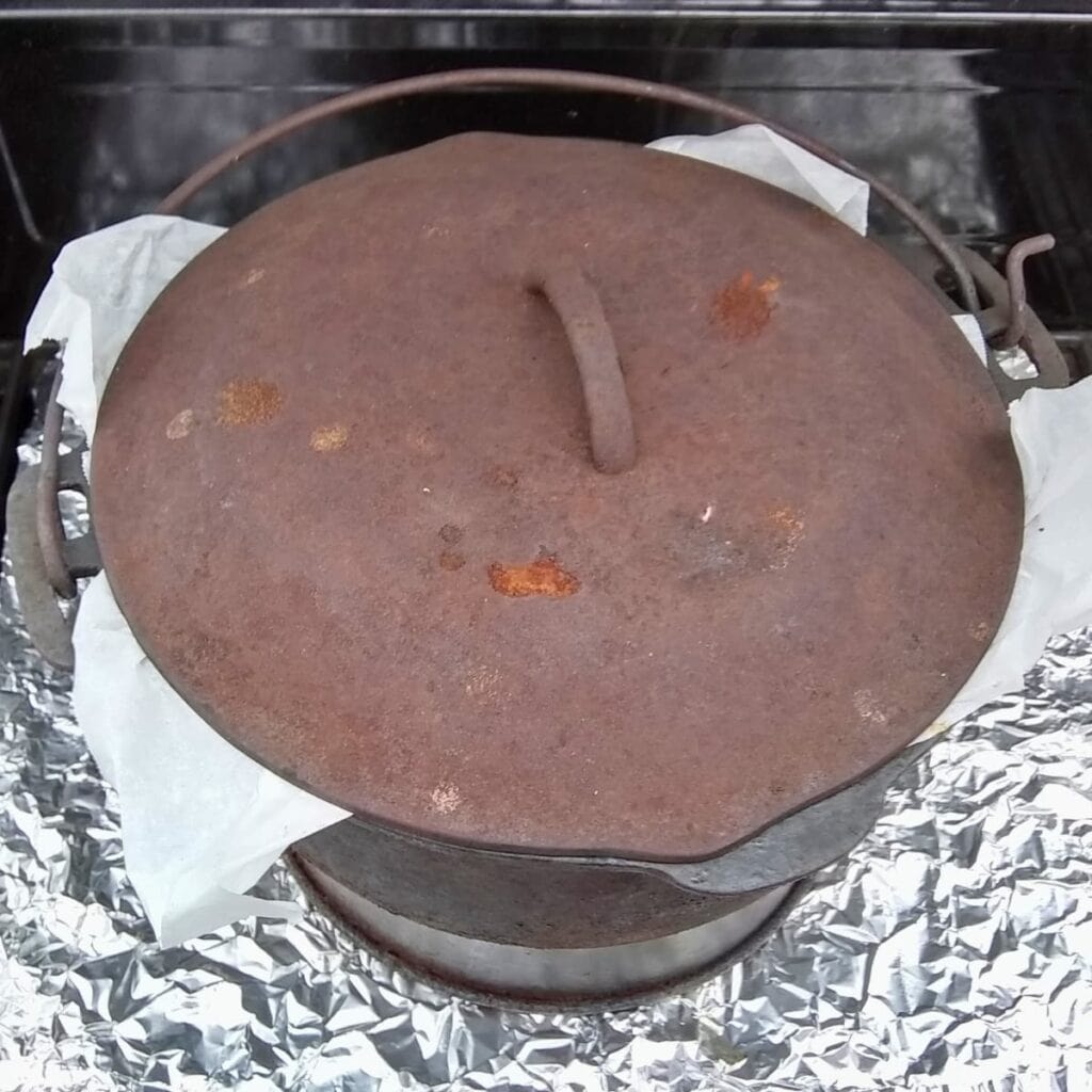 photo shows a dutch oven on a cake ring in a bbq grill with the lid on and parchment corners sticking out.