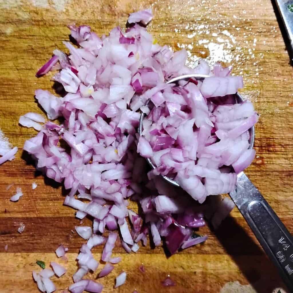 chopped onions on a cutting board with a quarter cup measure.
