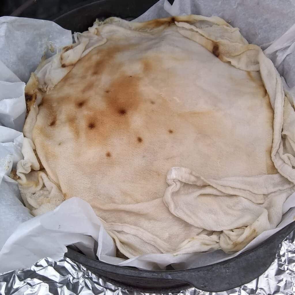 loaf of sourdough rye bread in a dutch oven covered with a piece of damp cloth.