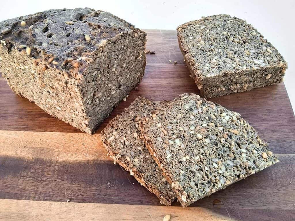 a chunk of seeded rye bread with spelt on a cutting board. Some of it is sliced.