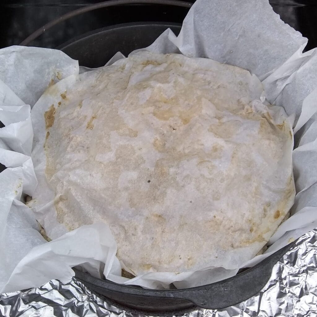 a piece of parchment has been placed on top of a sourdough loaf in a dutch oven.