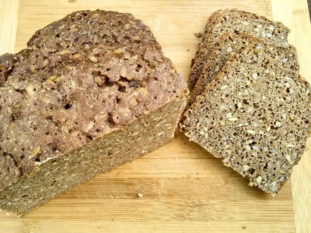photo of a loaf of sourdough rye bread with a few slices cut next to it on a cutting board.