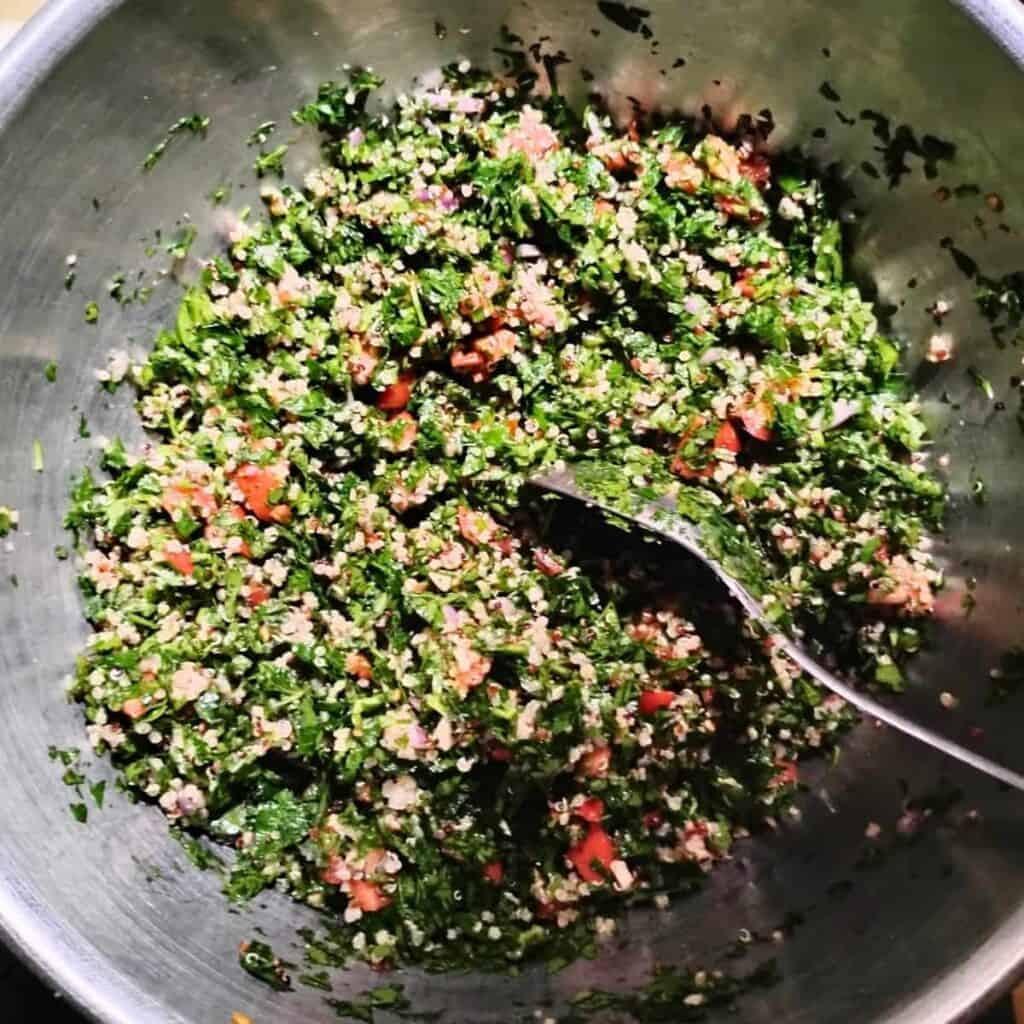 a mixing bowl filled with fresh tabouli salad and a spoon in it. 