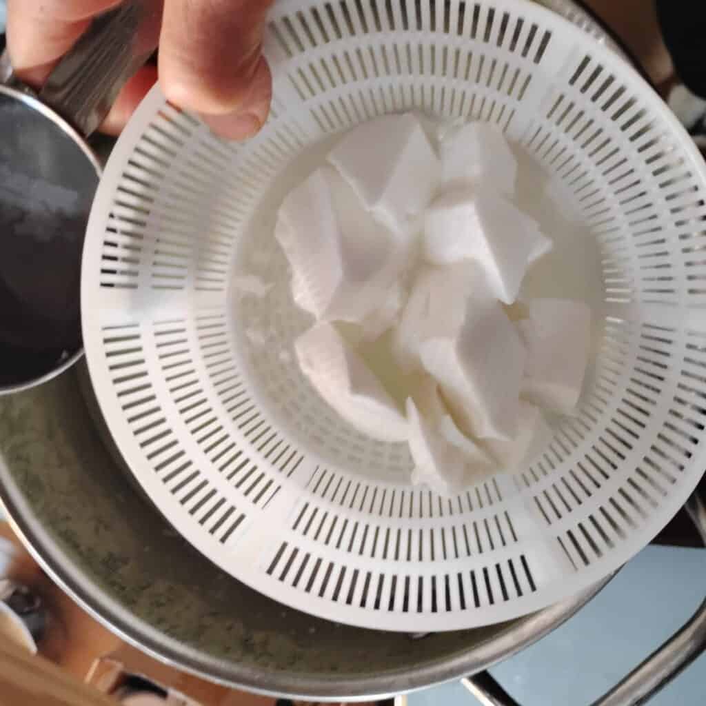 a person's hand is holding a basket with cheese curds over pot.