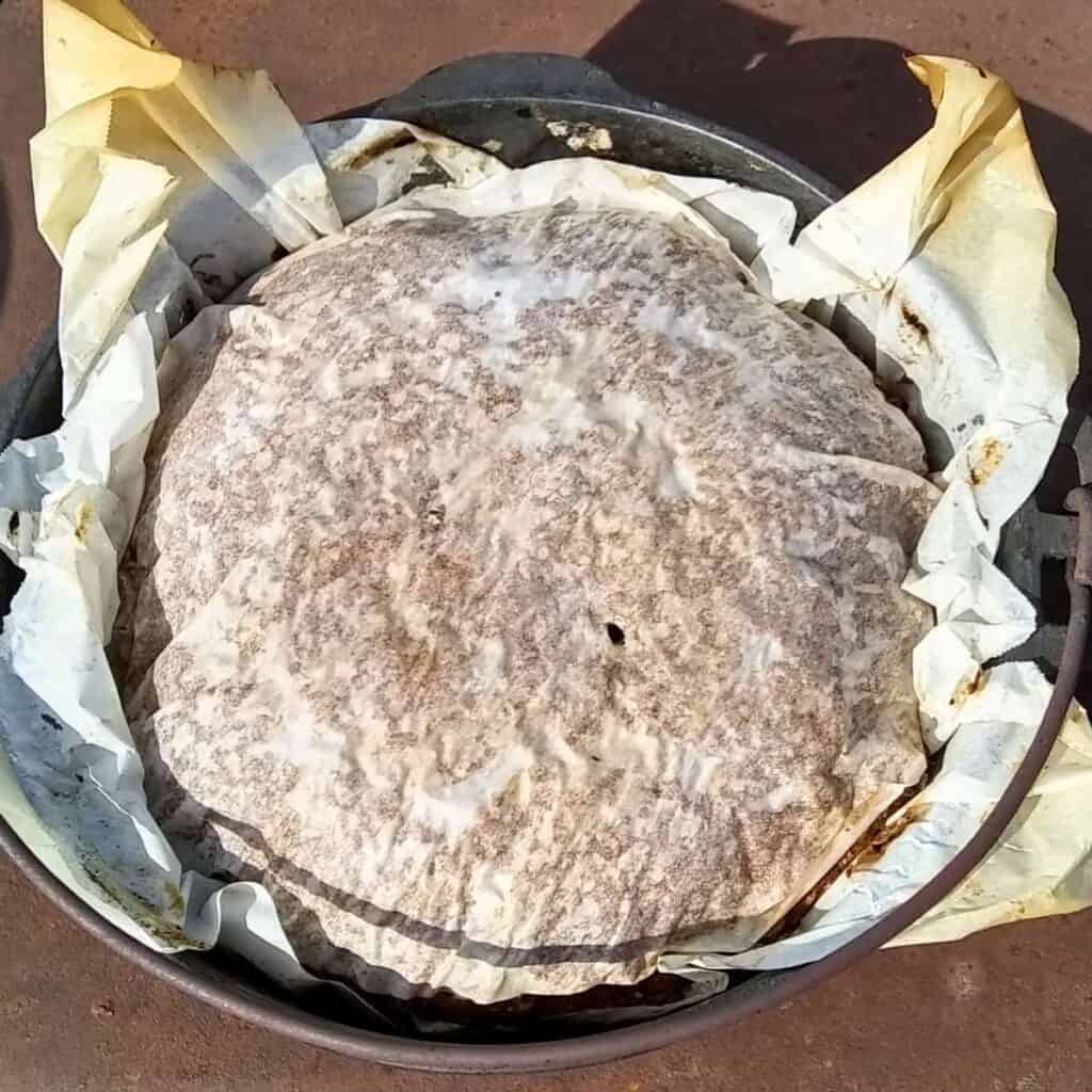 a loaf of breaf covered with a piece of parchment in a dutch oven.