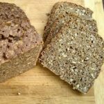 a chunk of sourdough no-knead seeded rye bread with spelt on a cutting board with a few cut slices next to it.
