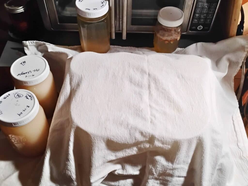 a feta draining station covered with a cheese cloth and two jars filled with brine sitting next to it.