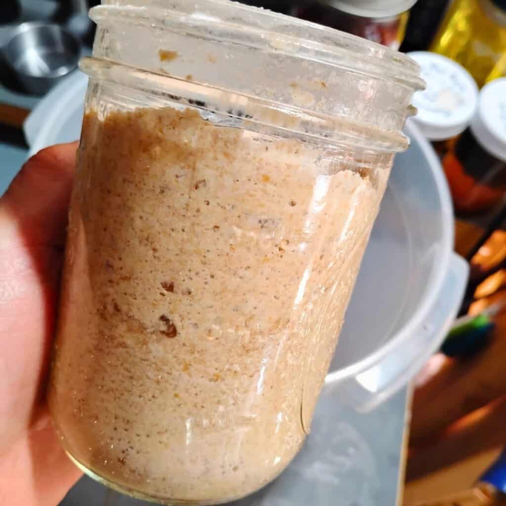 a pint mason jar filled with bubbly active sourdough in a person's hand.