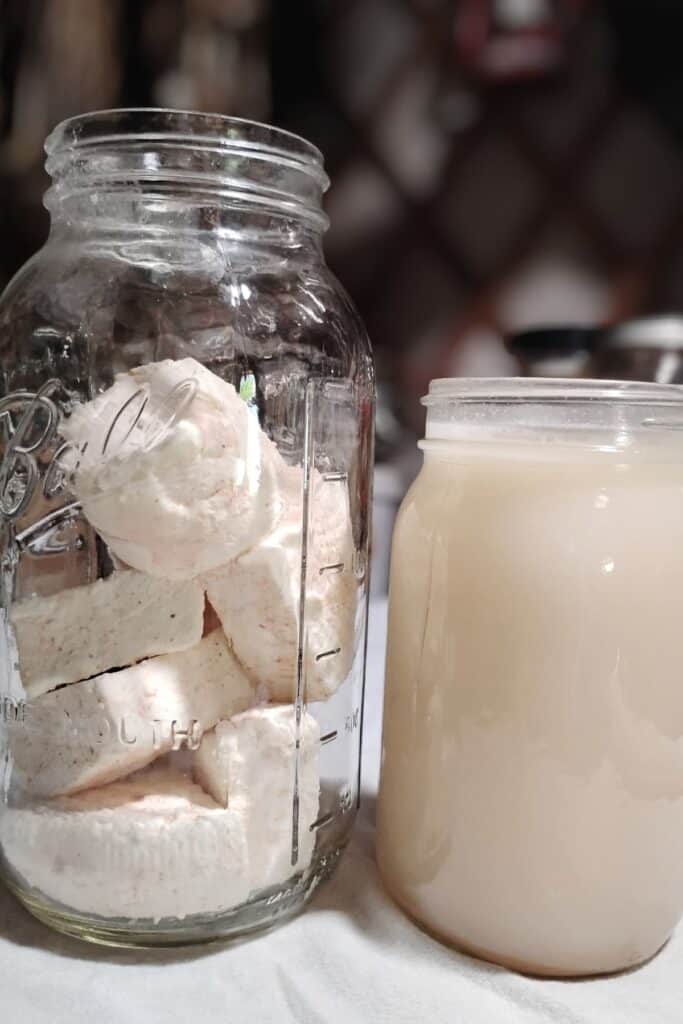 a jar filled with feta cheese chunks and a jar filled with salted brine beside it.