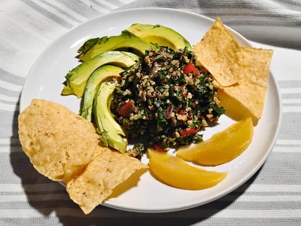 A plate with quinoa tabouli salad in the center and surrounded with corn chips, avocado slices, and fermented lemon slices. 