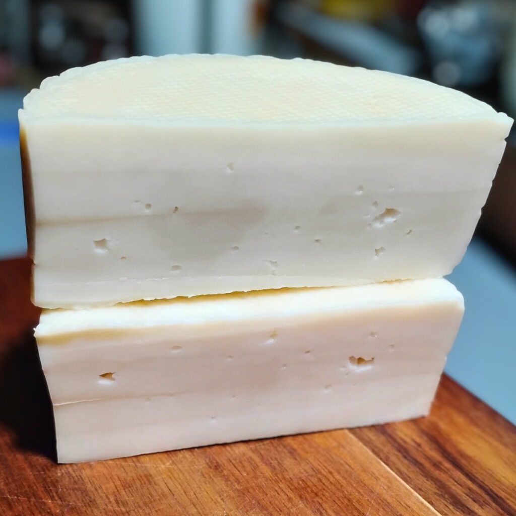 A stack of two halves of a bel paese cheese loaf on a cutting board.