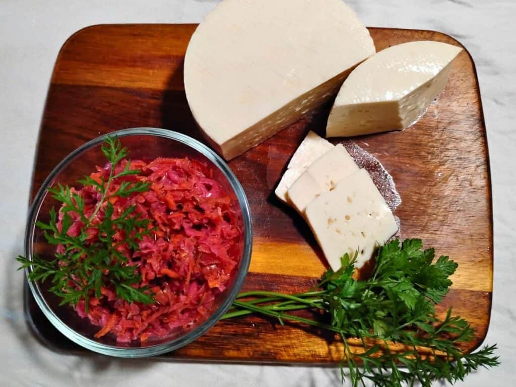 Bel paese cheese on a cutting board with some fermented coleslaw and parsley and carrot tops.