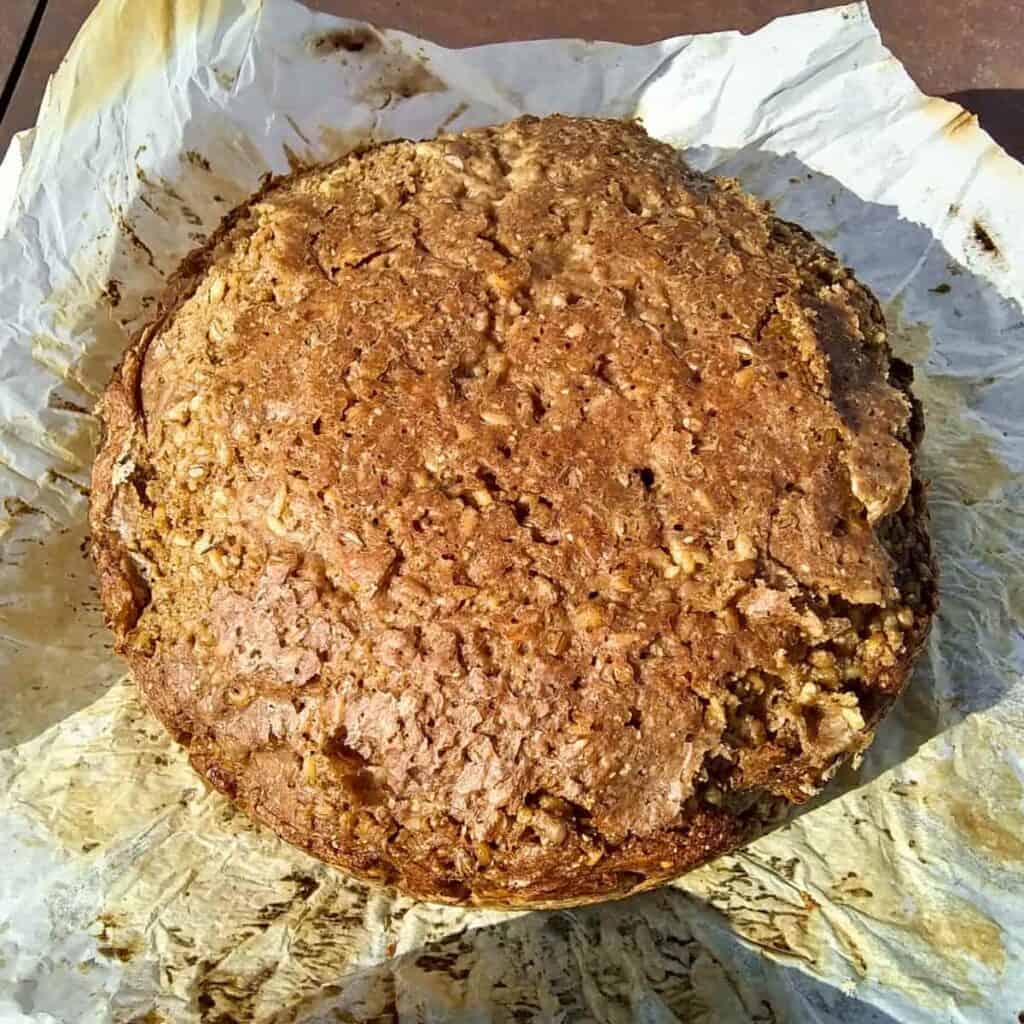 photo of a freshly bake whole loaf of no-knead sourdough seeded rye bread with spelt on a piece of parchment.